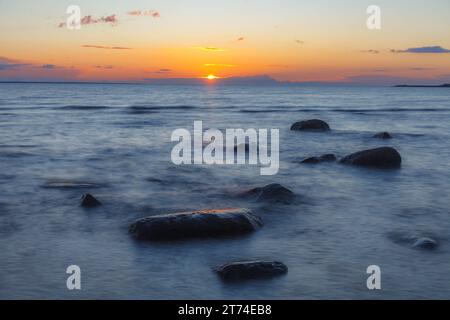 Evening at the shore of Baltic sea. Bright sunset and sea waves. Erratic boulders. Long exposure. Stock Photo