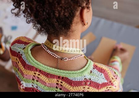 Back head view of young African American craftswoman in handmade knitted pullover working with sewing patterns by workplace Stock Photo