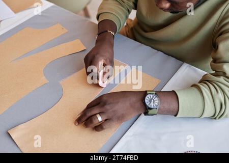 Young male tailor with piece of chalk in hand contouring paper patterns on grey textile while creating attire for new fashion collection Stock Photo