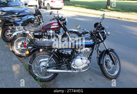 Three motorcycles parked on the side of a busy urban street in front of a large parking lot Stock Photo