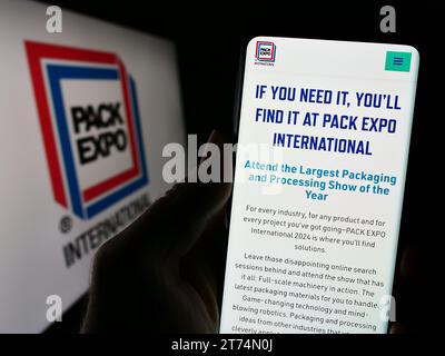 Person holding cellphone with website of US trade fair PACK EXPO International in front of business logo. Focus on center of phone display. Stock Photo