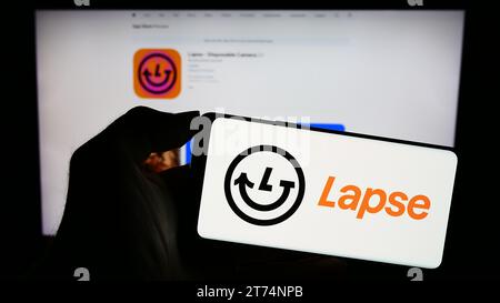 Person holding cellphone with logo of disposable camera app Lapse in front of webpage. Focus on phone display. Stock Photo