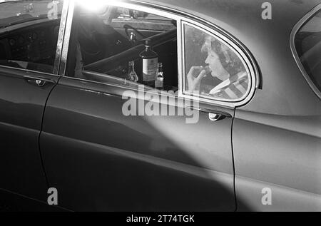 1970s Derby Day UK.  In the car park and before the Off, a racegoer enjoys a Gordon's Special Dry London Gin and tonic and a cup cake in the back of the Jaguar. Epsom Downs, Surrey, England 3rd June 1970.  HOMER SYKES. Stock Photo