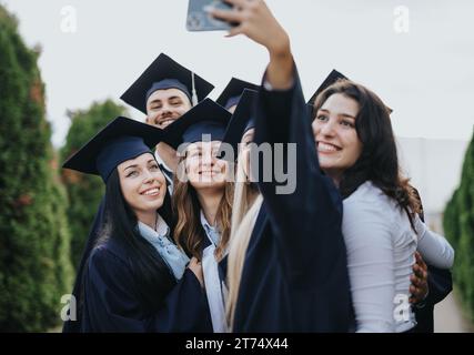 Group of university graduates celebrating their achievement in the park. They share happy moments, take selfies, and congratulating each other. Stock Photo