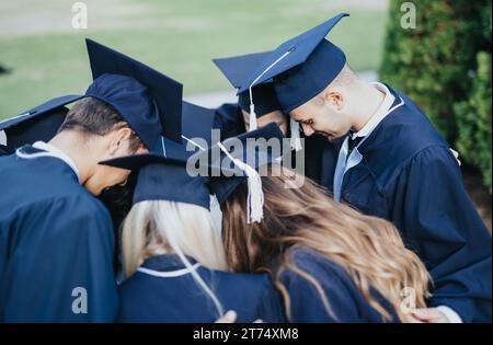 Large group of students wearing gowns and caps talking to each other while standing together in a circle, smiling and congratulating each other. Stock Photo