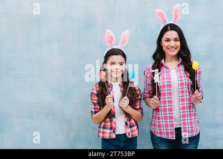 Mother daughter wearing bunny ears holding easter eggs bunny props Stock Photo