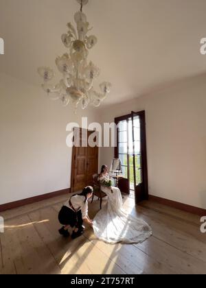 Rome, Italy - 09 august 2023: Girl-photographer adjusts the long train of the wedding dress to the bride sitting on a chair Stock Photo