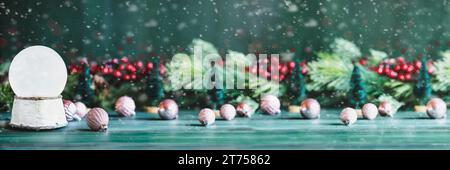 Banner of a magical empty snowglobe over a green rustic table background with falling snow. Christmas decorations in the background. Stock Photo