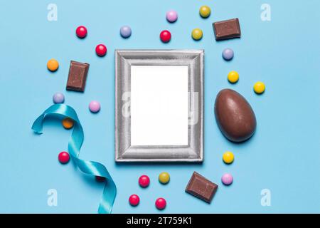 Empty blank white silver frame surrounded with easter egg gem candies chocolate pieces blue backdrop Stock Photo