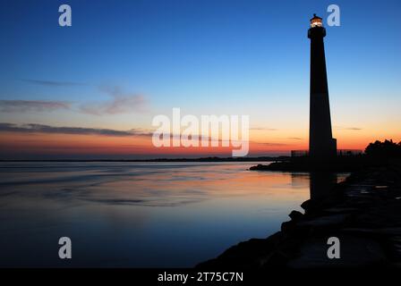 The bright dawn sky renders the Barnegat Lighthouse in silhouette except for the light beacon at the top Stock Photo