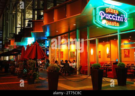 A large neon sign is illuminated at a restaurant and bar in Columbus Indiana while the customers eat al fresco Stock Photo