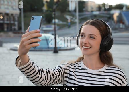 Smiling woman in headphones taking selfie on city street Stock Photo