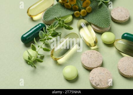 Different pills and herbs on light green background, closeup. Dietary supplements Stock Photo
