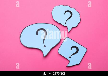 Different paper speech bubbles with question marks on pink background, flat lay Stock Photo