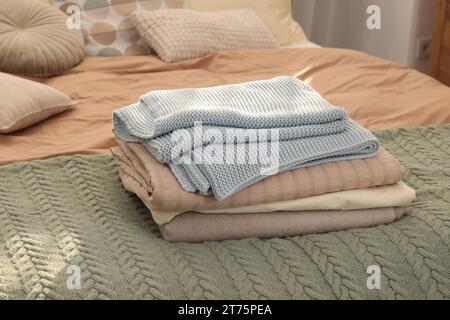 Stack of different folded blankets on bed indoors. Home textile Stock Photo