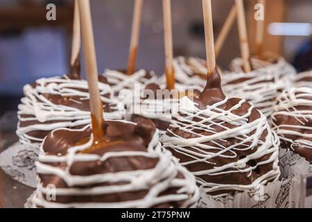 Several chocolate dipped caramel apples with a white chocolate drizzle arranged in a display at a market during the winter holidays. Stock Photo