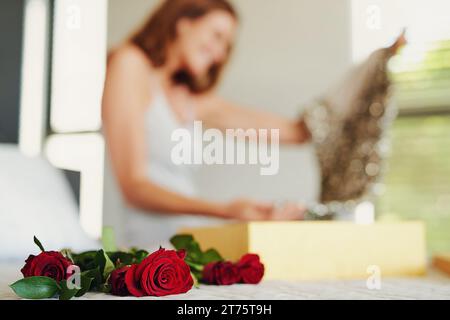 Woman, roses and box with gift in bedroom on birthday, celebration and valentines day event in home. Girl, dress and fashion with bouquet, flowers and Stock Photo
