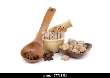 Wooden mortar filled with cinnamon sticks, star anise in a wooden spoon and brown sugar cubes in a wooden bowl isolated on white background Stock Photo