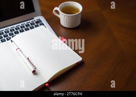 Notepad on top of laptop and next to a cup of tea. Wood table, copy space. Stock Photo