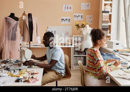 Two young African American fashion designers working in atelier while one of them using sewing machine against colleague creating embroidery Stock Photo