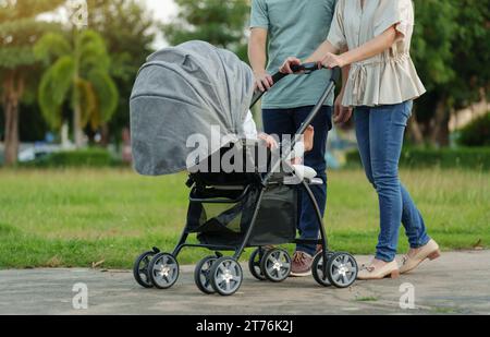 parent (father and mother) pushing infant baby stroller and walking in the park Stock Photo