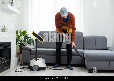 Dry cleaner's man employee removing dirt from furniture in flat, closeup, vacuum clean sofa with professional equipment. Stock Photo