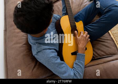 Biracial man sitting on sofa playing guitar at home Stock Photo