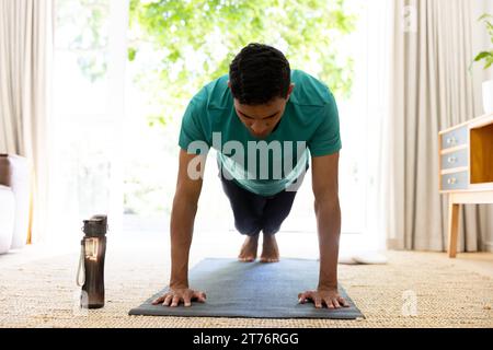 Biracial man exercising and doing push ups on mat at home Stock Photo
