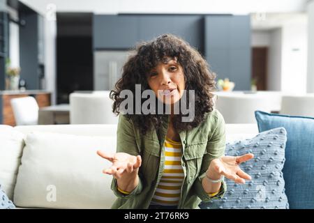 Happy mature caucasian woman having video call, talking and gesturing on couch in sunny living room Stock Photo