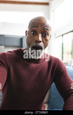 Surprised african american mature man having video call, gasping in sunny living room at home Stock Photo