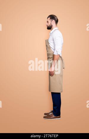 Full size fullbody, side view profile portrait snap of handsome attractive barber in uniform, isolated over grey background Stock Photo