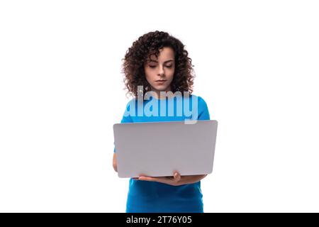 casual young curly woman in a blue t-shirt works as a programmer and holds a laptop Stock Photo