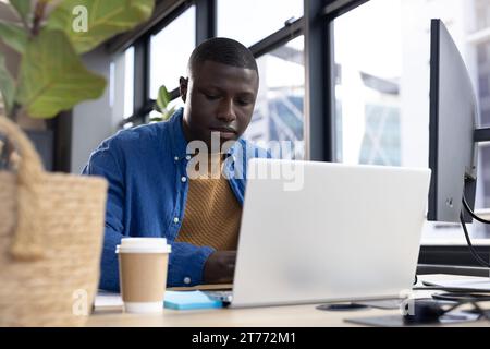 Focused african american casual businessman using laptop sitting at desk in office Stock Photo