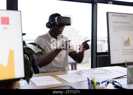 African american casual businessman wearing vr headset using virtual interface at office desk Stock Photo