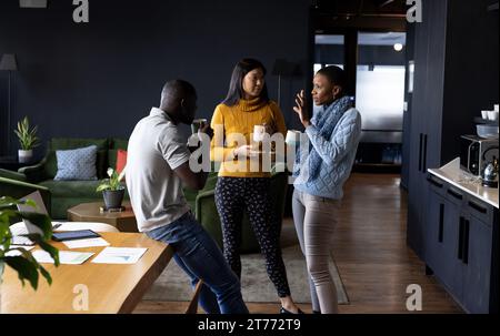 Happy diverse male and female colleagues having coffee and talking standing in office Stock Photo