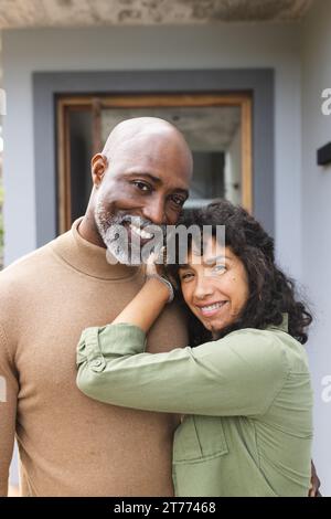 Portrait of happy mature diverse couple smiling and embracing on terrace outside house Stock Photo