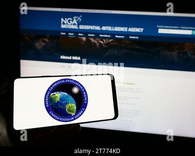 Person holding cellphone with seal of US National Geospatial-Intelligence Agency (NGA) in front of webpage. Focus on phone display. Stock Photo