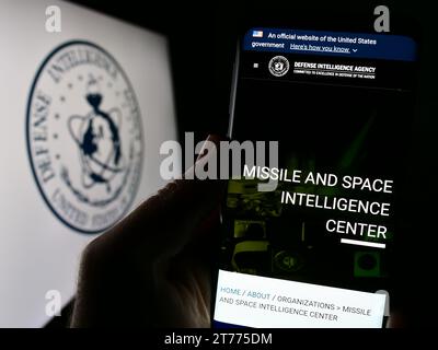 Person holding smartphone with webpage of United States Defense Intelligence Agency (DIA) in front of logo. Focus on center of phone display. Stock Photo