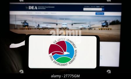 Person holding cellphone with seal of United States Drug Enforcement Administration (DEA) in front of webpage. Focus on phone display. Stock Photo