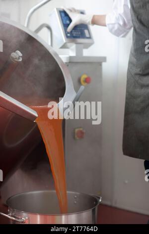 Factory worker using computer controlled machinery pouring tomato sauce into a pan Stock Photo