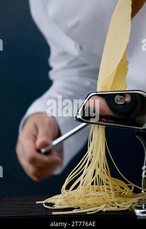 Close up of a chef hand turning the handle of a pasta maker with tagliolini coming out Stock Photo