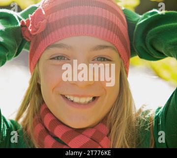 Smiling young girl with her hands on her head wearing a woolly hat Stock Photo