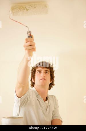 Portrait of a man painting the ceiling with a paint roller Stock Photo