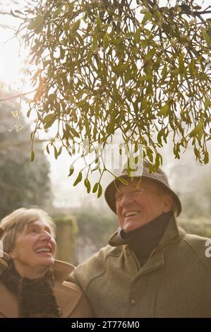 Mature couple standing under a tree looking up and smiling Stock Photo