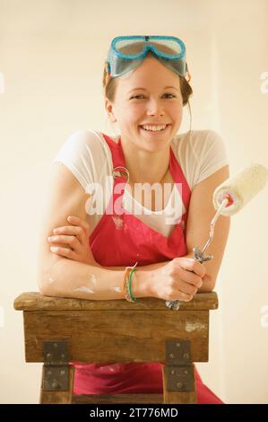 Portrait of a smiling woman standing on a ladder holding a paint roller Stock Photo