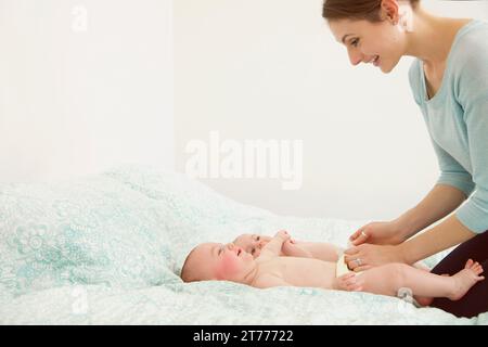 Smiling Mother Kneeling on Bed Playing Twin Babies Stock Photo