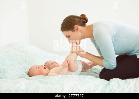 Mother Kneeling on Bed Kissing Twin Babies Stock Photo