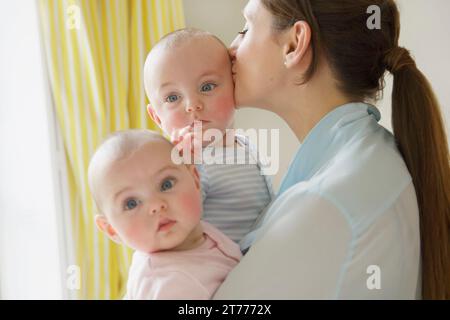 Mother Kissing Twin Babies Stock Photo