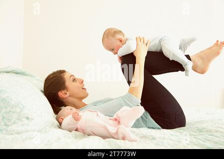 Mother Lying on Bed Playing with Twin Babies Stock Photo