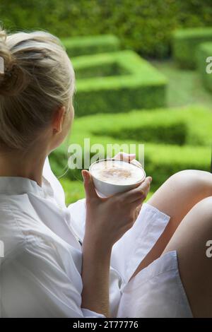 Woman Having Cappuccino Looking Out into Garden Stock Photo